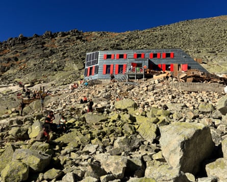 A hut with red windows on a rocky mountain side