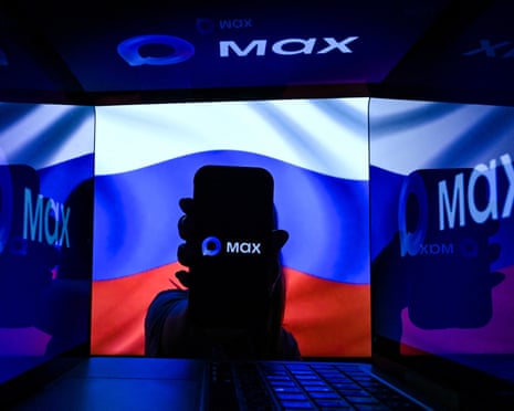 A person holding a smartphone with the Russian messenger and e-commerce app logo Max displayed on its screen, while standing in front of a Russian flag, in Moscow