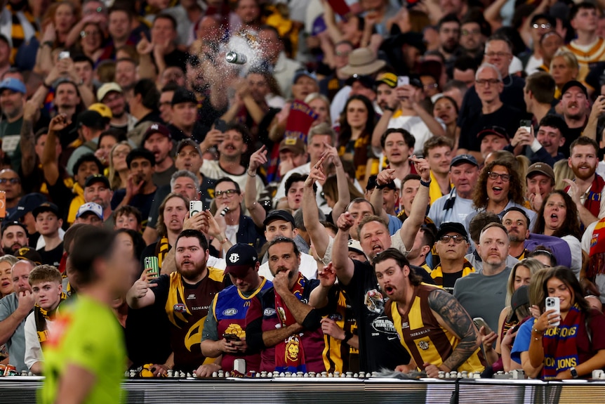 A can is seen hurtling towards AFL umpires after the Hawks' AFL final loss to Brisbane.