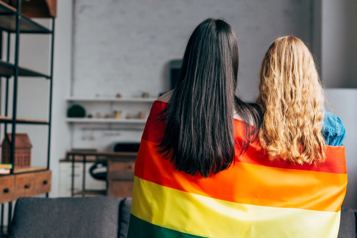 Casal de lésbicas envolto em uma bandeira do arco-íris. Metrópoles