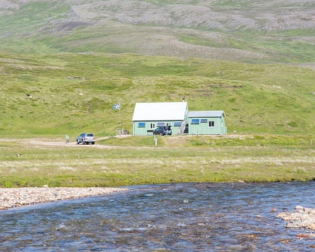 Small buildings with cars parked outside, with a grassy landscape and flowing water nearby