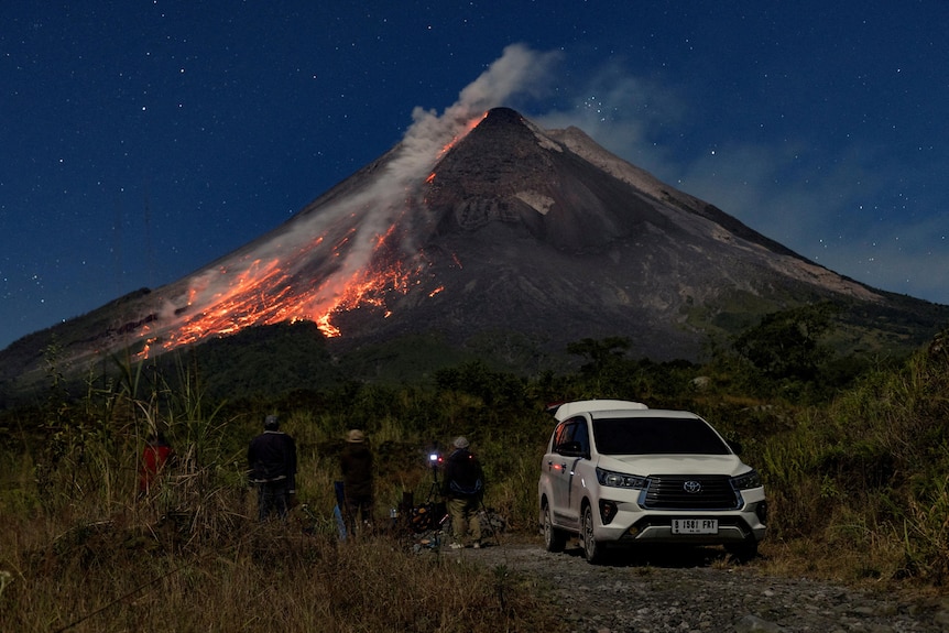 People watch as Mount Merapi volcano spews hot lava and steam