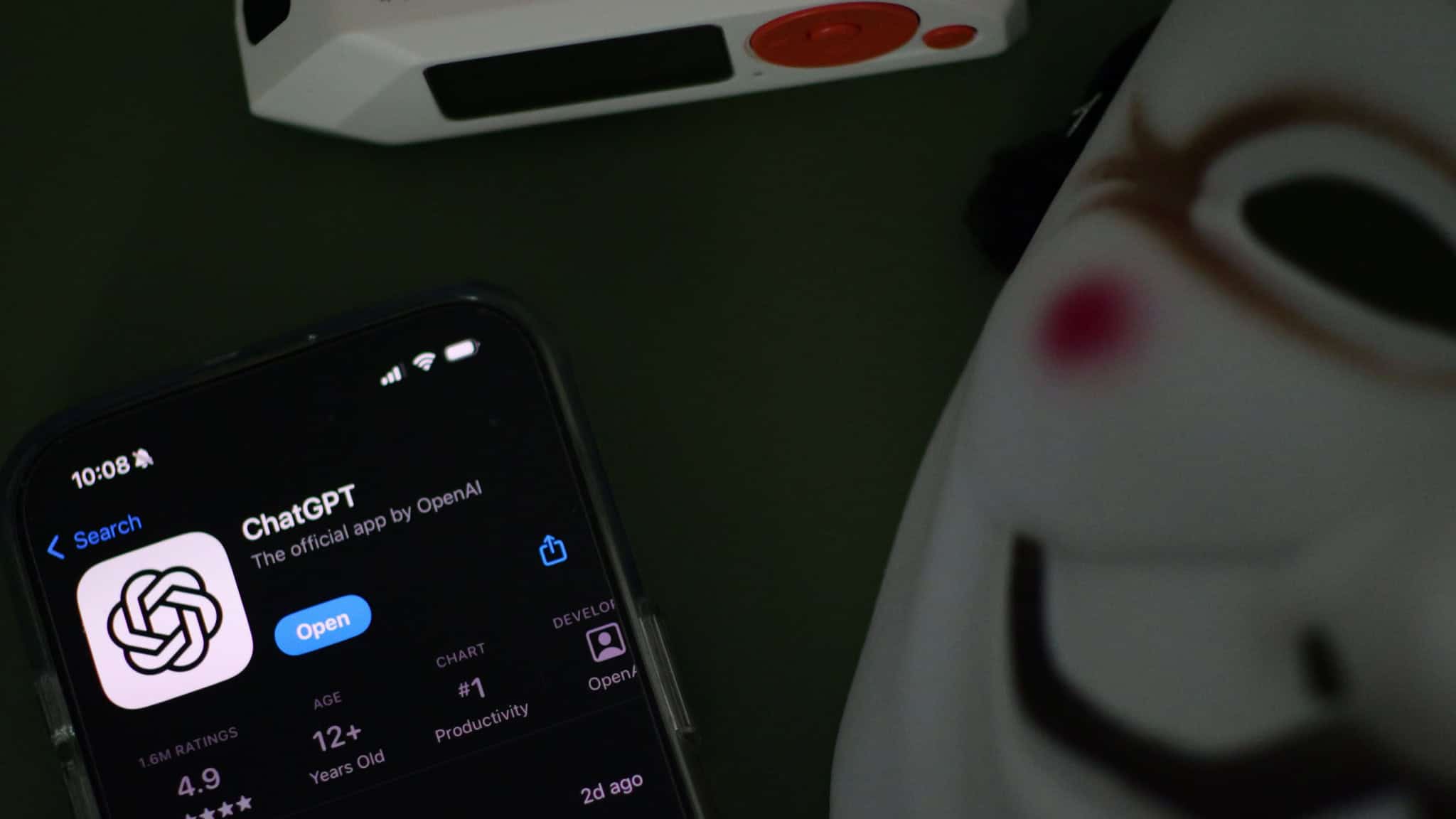 Página do aplicativo ChatGPT na App Store aberta num iPhone colocado do lado de uma máscara de Guy Fawkes