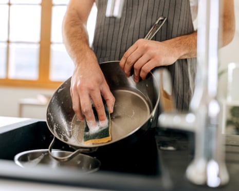 Man uses a scrubber sponge to clean a kitchen pan in sink