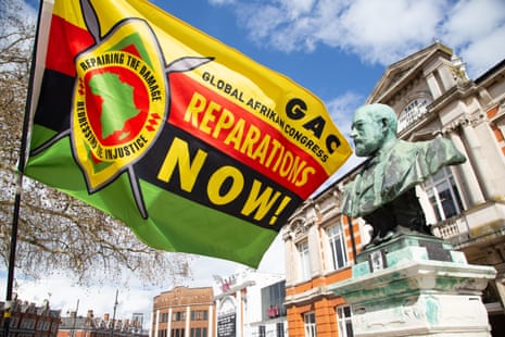A flag reading "Reparations Now!" flies above buildings during a Windrush commemoration event