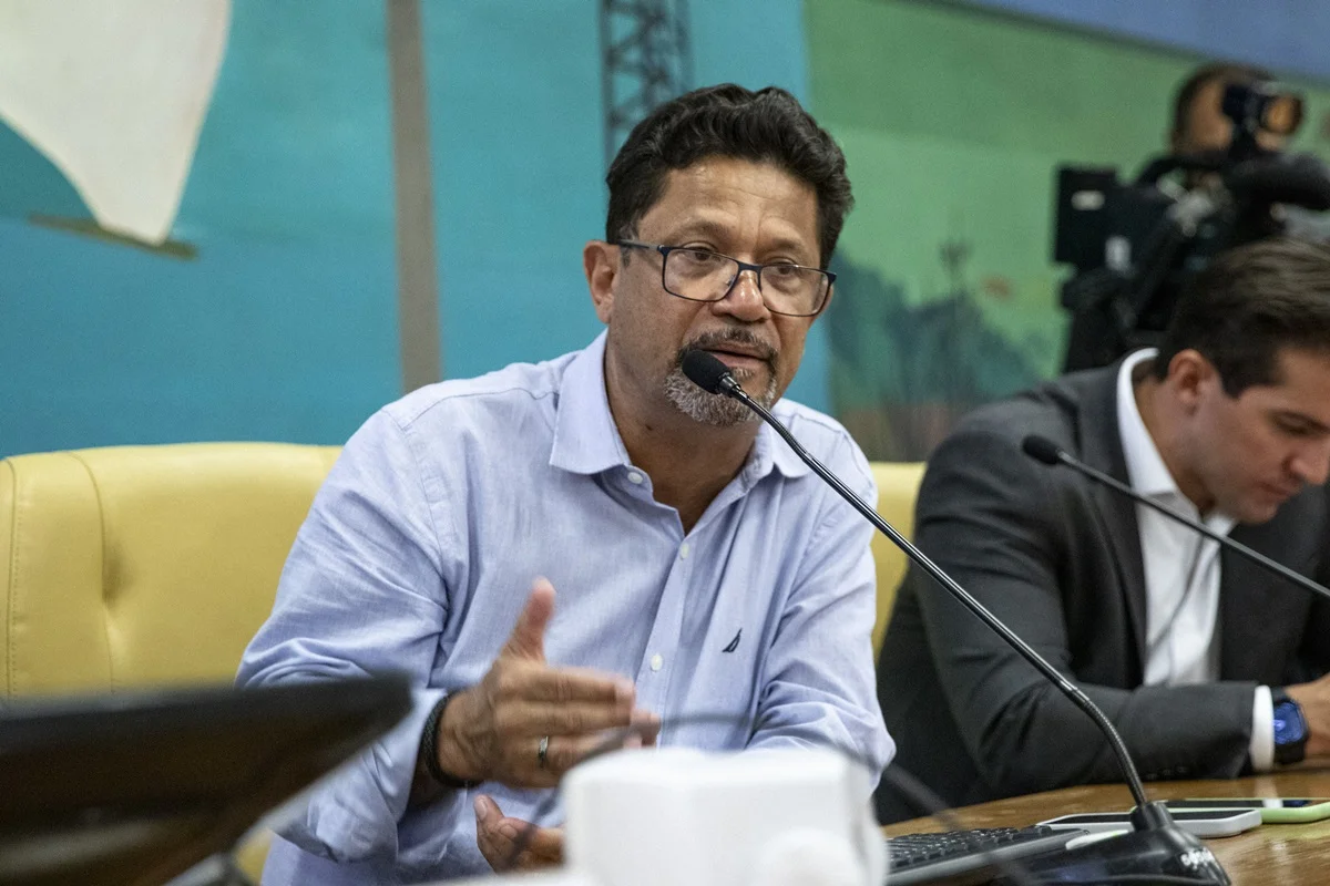 Imagem colorida mostra Isac Félix, homem pardo, de óculos e camisa azul clara, sentado em uma mesa falando ao microfone sobre Sabesp - Metrópoles